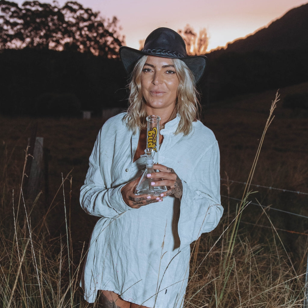 Woman presenting the Bud Beaker Bong 25cm at sunset